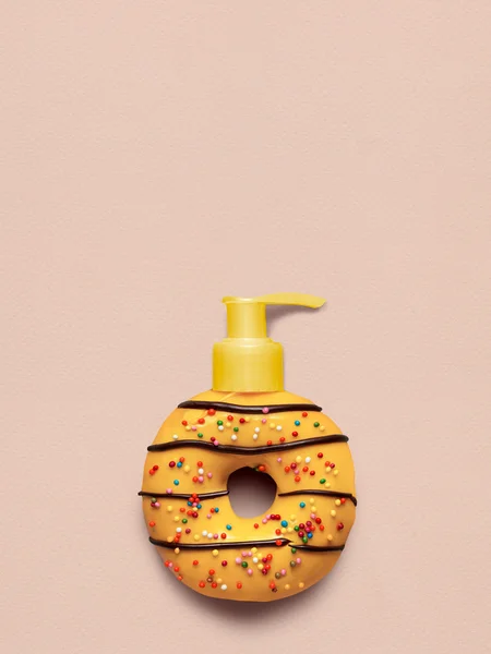 Donut with dispenser. Creative still life of a tasty sweet yellow donut with a cosmetic pump dispenser on pink background.