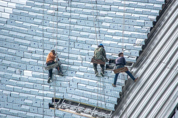 Mans  installing windows of high rise building glass facade.