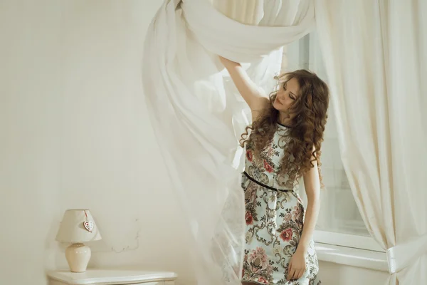 Attractive woman with curly hair removing the curtain