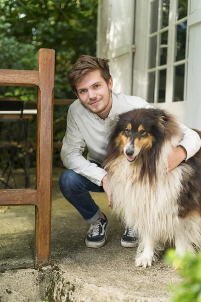 Cute young man kneeling with hairy collie dog outdoors