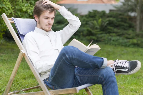 Cute bearded young man reading a book in the garden