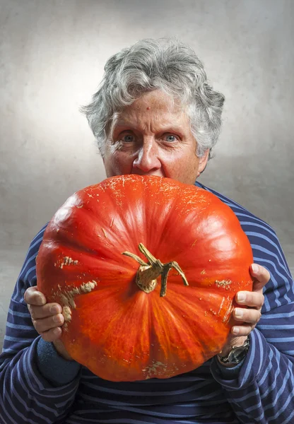 Scary old woman eating a big ripe pumpkin. Halloween theme.