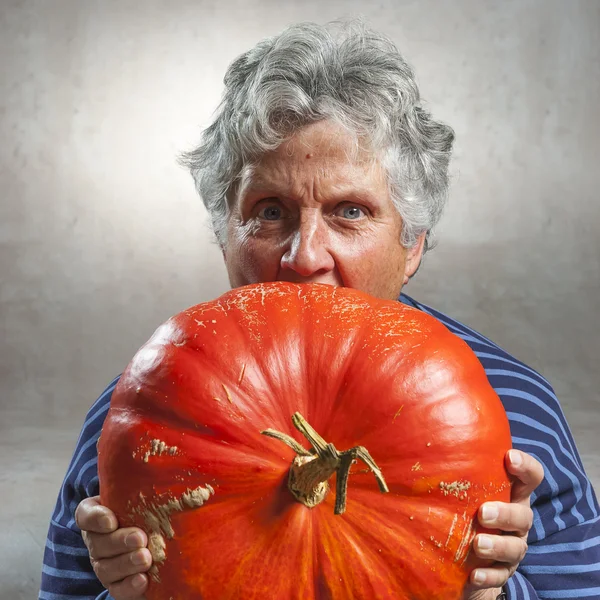 Closeup of scary old woman eating a big ripe pumpkin