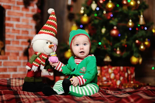 A child dressed as an elf sitting on a plaid background on the C