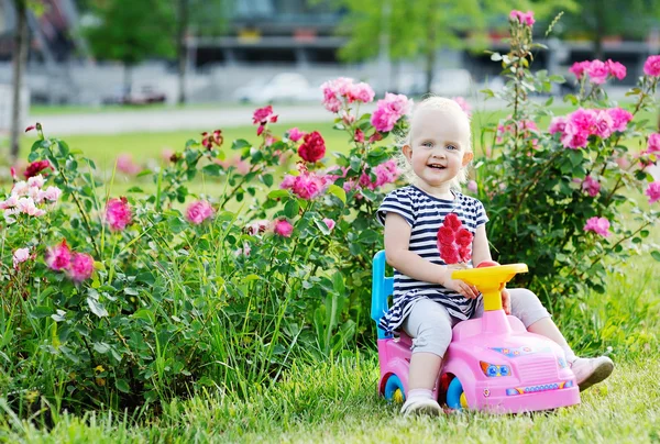 Baby girl driving pink toy car on a background of roses