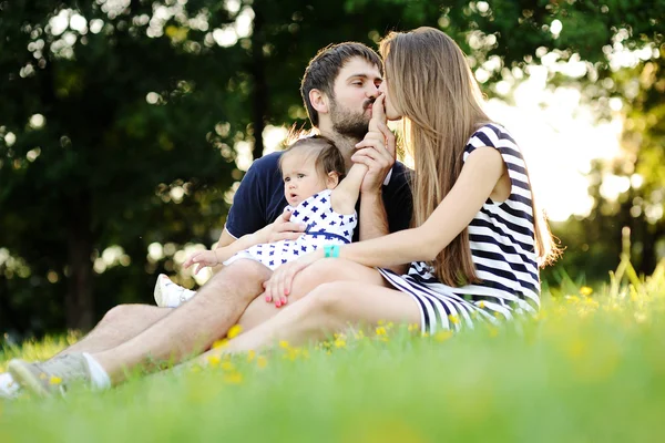 Young family relaxing in the park on the grass. Mom and dad kiss