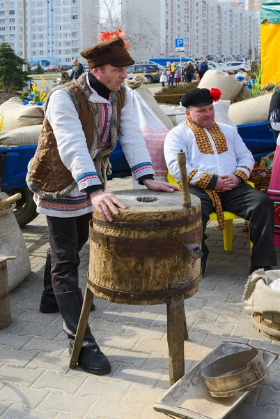 Man stands at old hand-mill during outdoors Shrovetide entertainment program