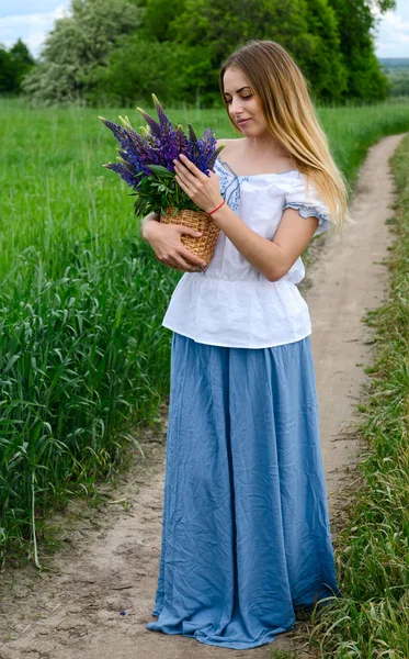 Beautiful girl with basket of wild flowers on rural road