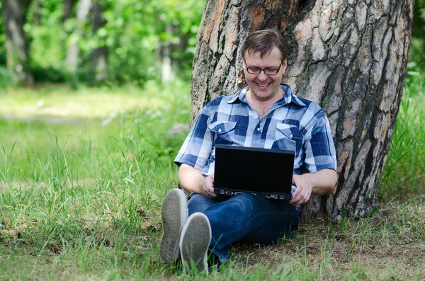 Man with laptop is resting in forest near old pine