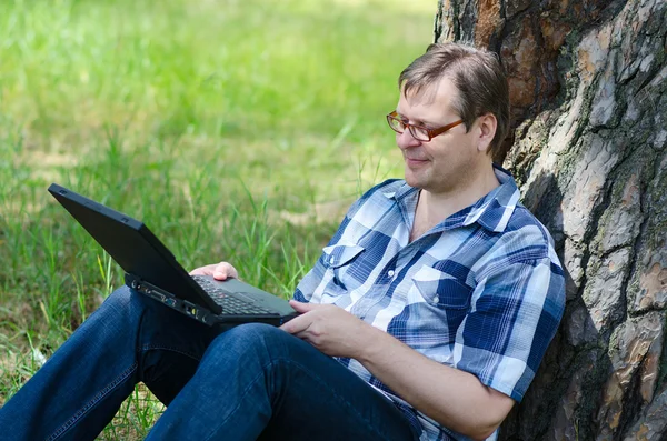 Man with laptop is resting in forest near old pine