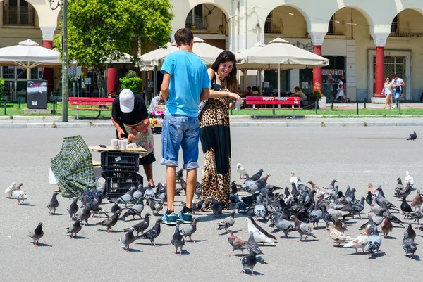 Young man and woman are feeding pigeons in square of Aristotle in Thessaloniki