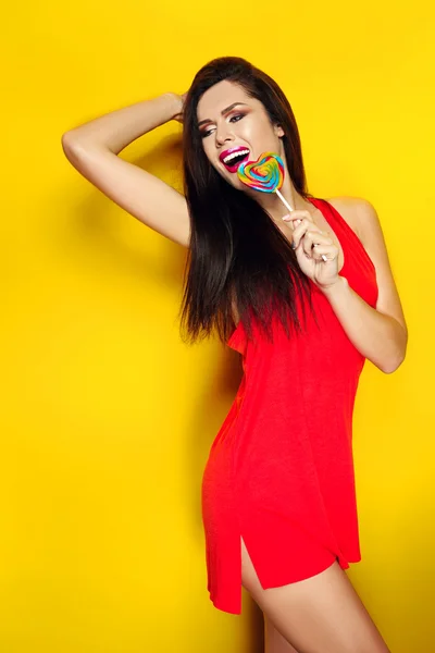 Beautiful young girl with candy in his hands smiling and posing for a photograph, a red T-shirt, beautiful and healthy hair, yellow background