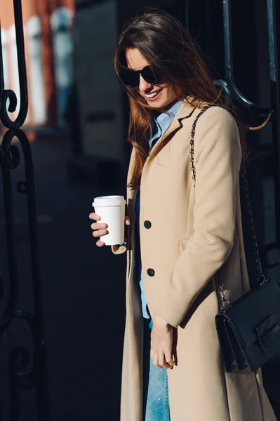 Beautiful and young girl in sunglasses drinking coffee in the street and walk around the city in the summer.