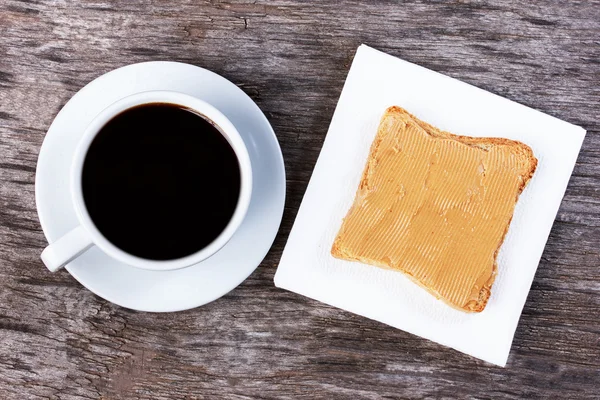 Sandwich with peanut butter on a paper napkin, cup of coffee on
