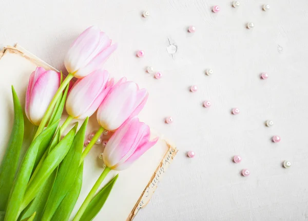 Pink tulips with heart and beads over white wooden table. Closeu