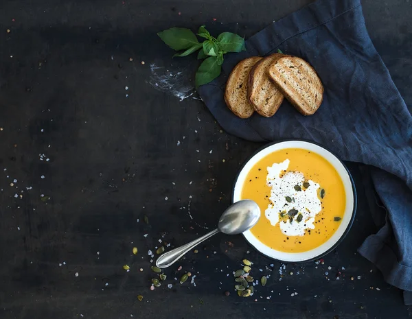 Pumpkin soup with cream, seeds, bread and fresh basil on grunge black background