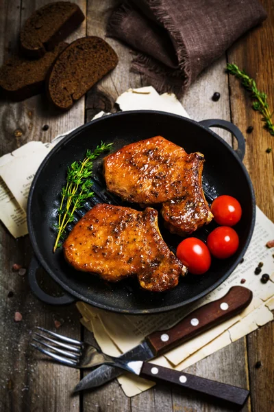 Grilled pork chops with thyme and cherry tomatoes in iron skillet