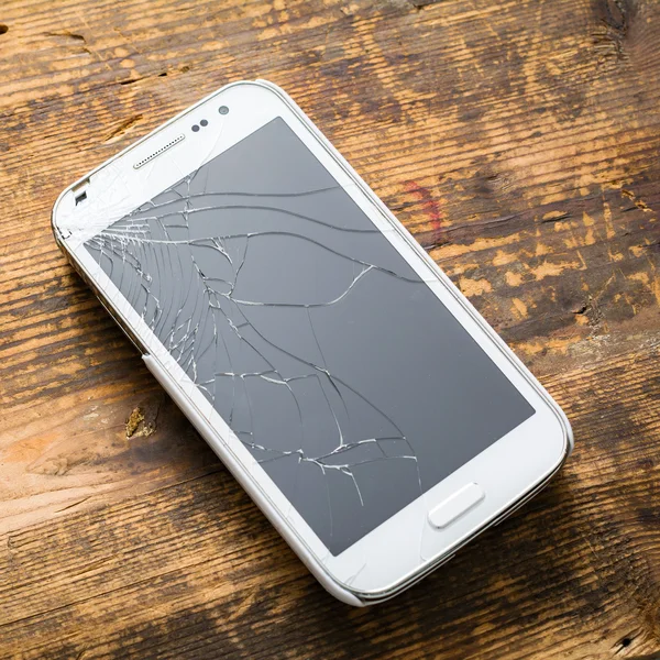 Smart phone with broken screen on wooden backdrop
