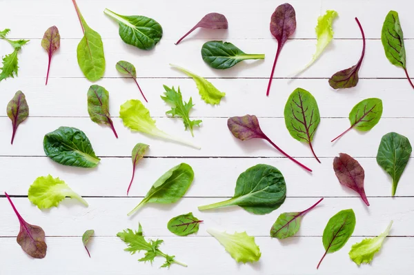 Various salad leaves on white wooden background. Flat lay