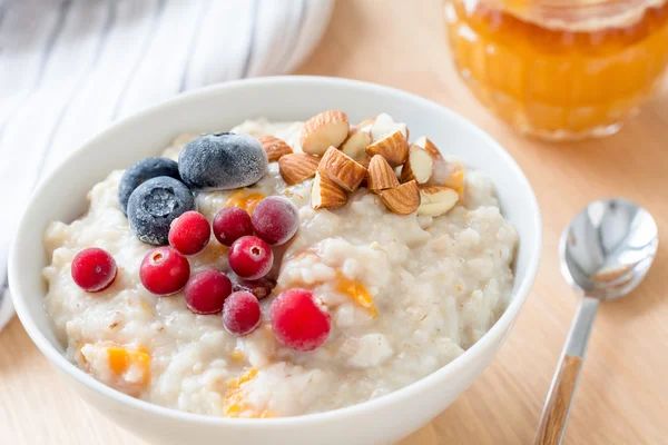 Oatmeal porridge with blueberries, cranberries and nuts in bowl on breakfast table. Close up