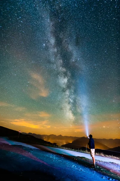 Man with a light standing at night with milky way
