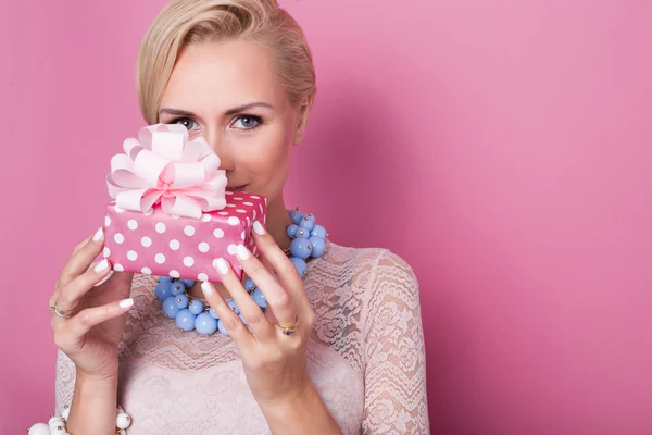 Merry christmas. Beautiful blonde woman holding small gift box with ribbon. Soft colors