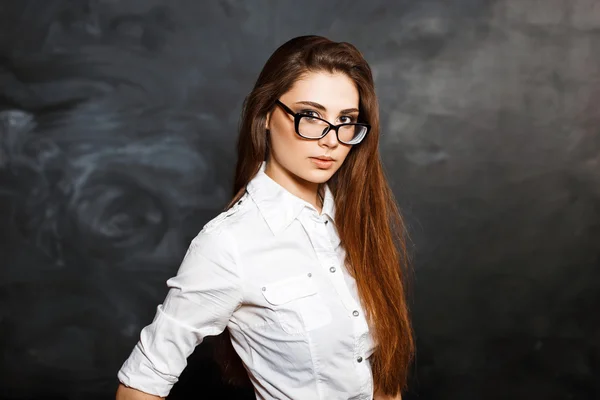 Close-up portrait of a young beautiful girl with stylish glasses and a white blouse on a dark background.