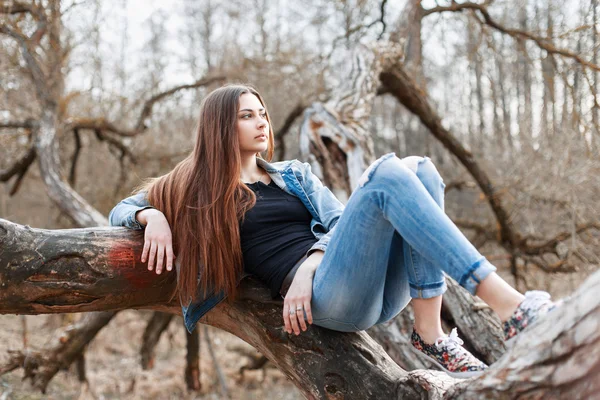 Young hipster girl with long hair and a denim jacket lying on a tree