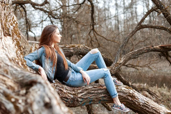 Beautiful young girl sits and dreaming on a tree branch.