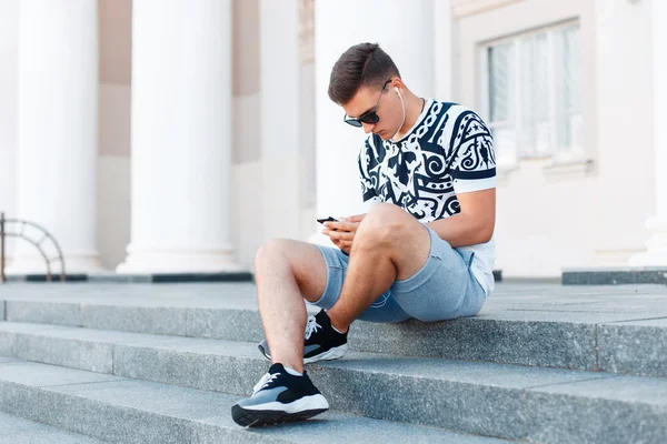 Young handsome man sitting on the steps and work on your phone.
