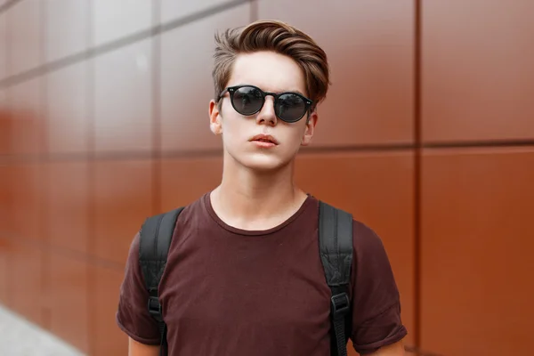Young handsome guy with hair in sunglasses standing near a wall