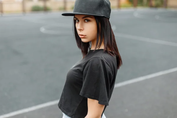 Young beautiful girl in a black baseball cap and t-shirt on the background of the stadium.