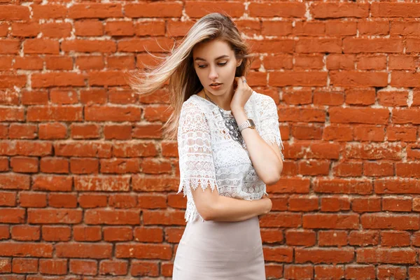 Beautiful stylish young girl in white vintage blouse on a background of red brick wall. Wind blows hair.