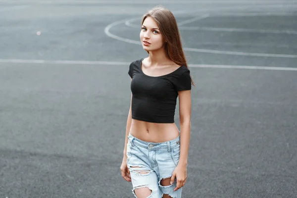 Pretty woman in a black T-shirt and torn jeans on the background of the stadium