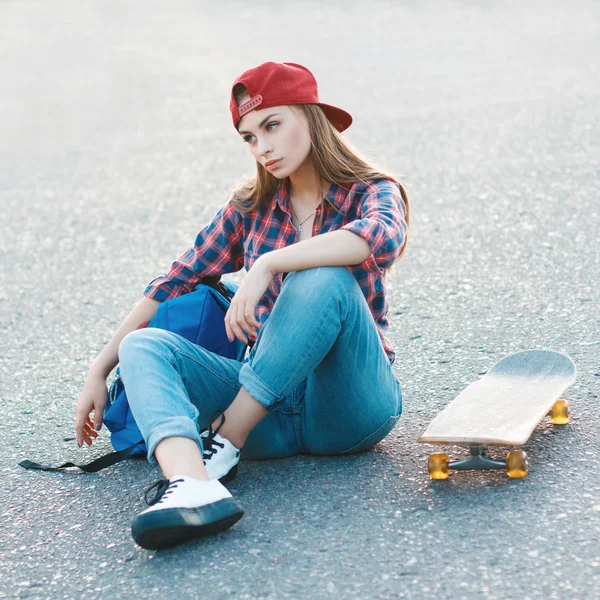 Portrait of a beautiful woman in a shirt and a baseball cap with a skateboard in the park.