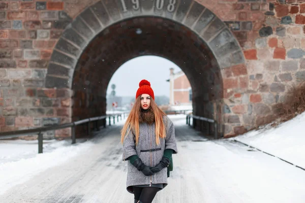 Young beautiful girl in winter clothes stands on the background of a stone arch