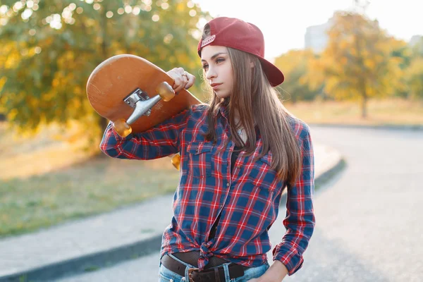 Young beautiful woman holding a skateboard in the park at sunset