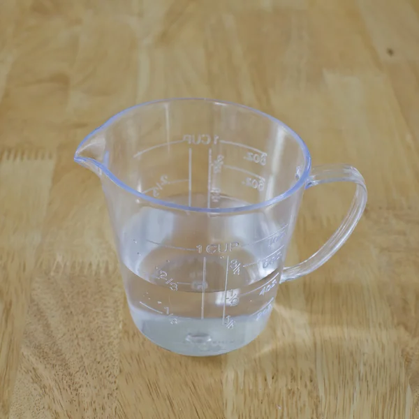 Warm water in measuring cup on a wood background