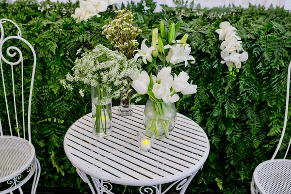 White flowers arrangement in glass vases on white metal desk.