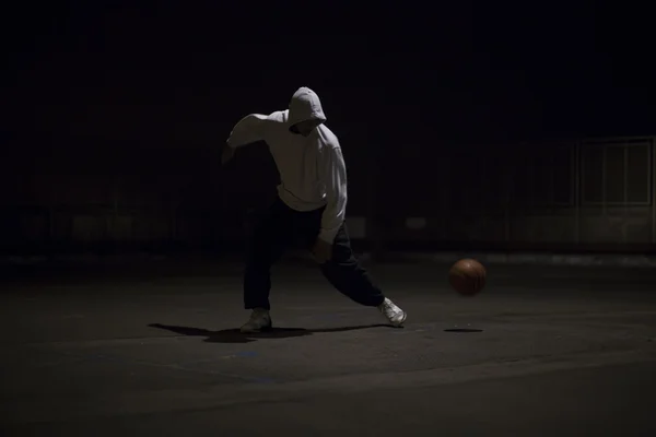 Hooded basketball player dribbling the ball at night under a street light