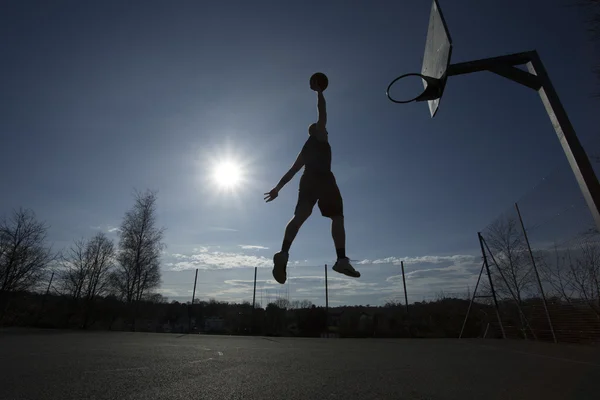 Silhouette Basketball player in mid air slam dunking on an outdoor basketball hoop