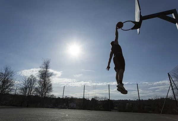 Silhouette Basketball player in mid air slam dunking on an outdoor basketball hoop