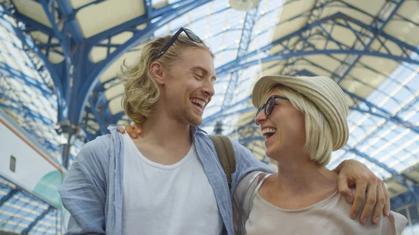 Attractive couple walk arm in arm in a train station whilst sharing a laugh together
