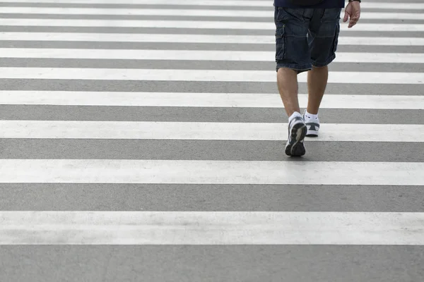 Legs of a man wearing shorts and sneakers walking across a zebra crossing