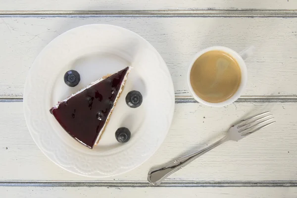 Breakfast: a blueberry cheesecake on a white wooden table and a coffee