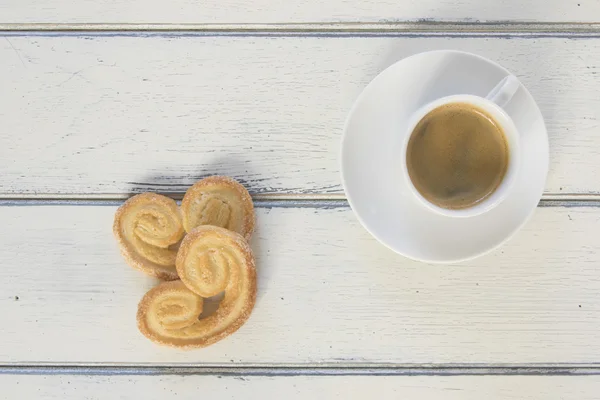 Breakfast: two puff pastry cookies on a white wooden table and a coffee