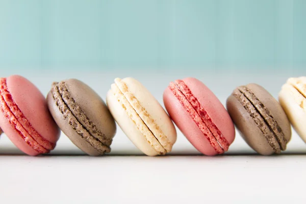 Chocolate, vanila and strawberry macaroons (aka macarons) on a white wooden table with a robin egg blue background. Vintage Style.