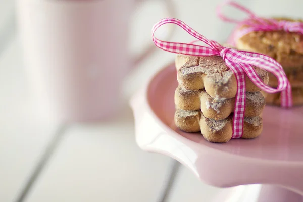 Cup and cookies tied with pink ribbon on a cake stand.