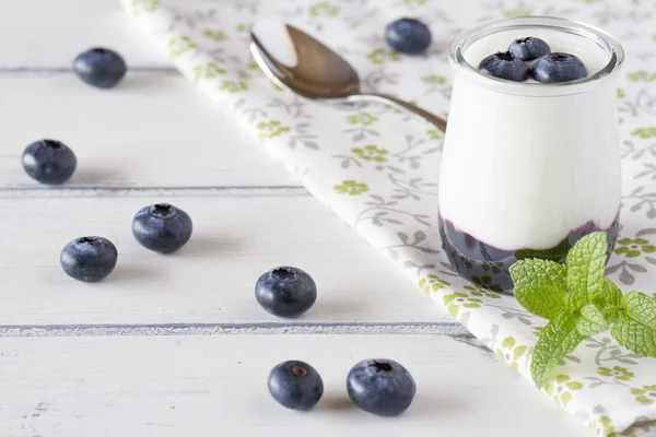 Jar with greek yogurt, blueberries jam and peppermint in a white wooden table