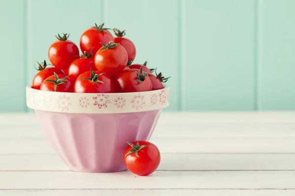 Several tomatoes in a pink bowl on a white wooden table with a robin egg blue background. Vintage look.